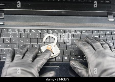 hands with gloves typing on laptop keyboard with padlock, cyberattack Stock Photo