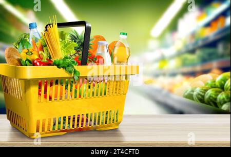 Food and groceries in shopping basket on wood table on blurred suppermarket aisle background Stock Photo