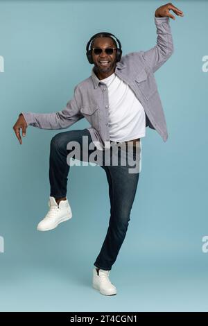 Smiling dark skinned man in headphones dancing making funny movements to music. Stock Photo