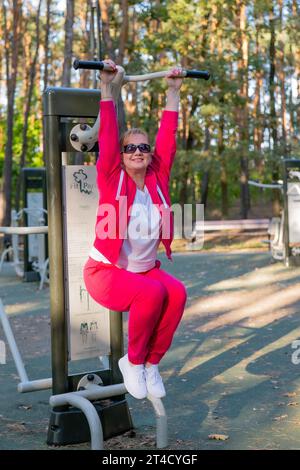 Portrait of a middle-aged woman doing pull-ups in the park Stock Photo