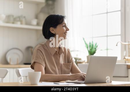 Smiling mature woman using laptop in domestic kitchen Stock Photo