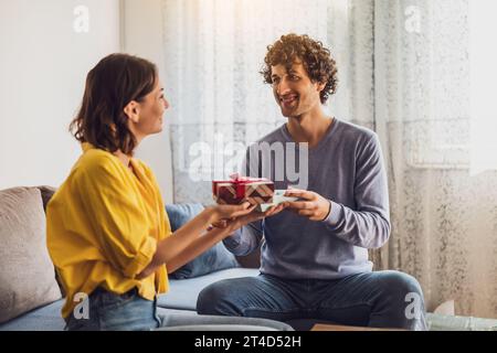 Portrait of young happy couple. Woman is giving gift to her man. Stock Photo