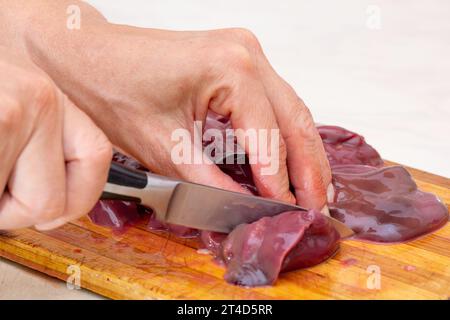 Woman hand cutting beef liver on cutting board using knife Stock Photo