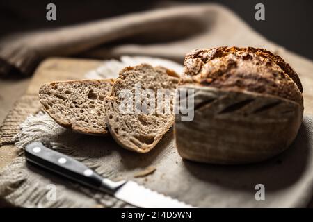 Fresh sourdough bread with a cut slice on a cutting board.. Stock Photo