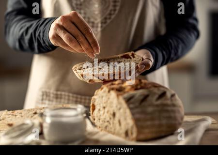 Female cook salting a fresh slice of bread - Close Up. Stock Photo