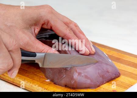 Woman hand cutting beef liver on cutting board using knife Stock Photo