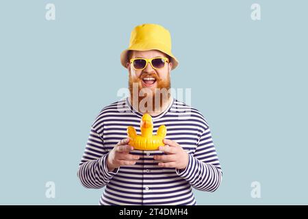 Funny chubby man with small toy inflatable duck on pastel light blue background. Stock Photo