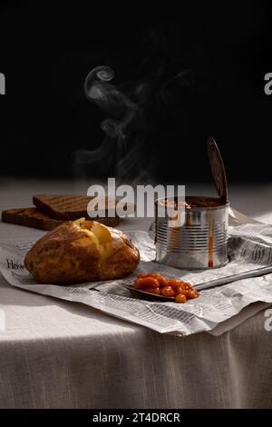 Steaming roasted jacket potato, baked beans in a tin can and toasts served on newspaper Stock Photo