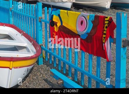 colorful beach towel hanging on fence beside a fishing boat, Cogoleto, Liguria, Italy Stock Photo