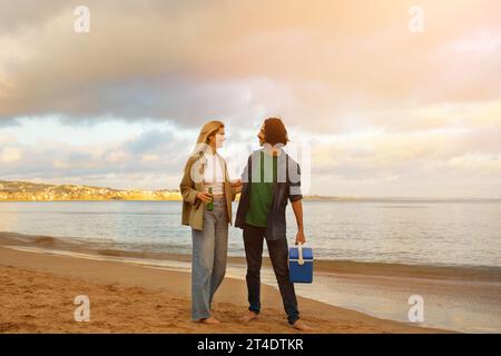 Affectionate Young Pair Having Walk On The Beach And Sipping Soft Drinks Stock Photo