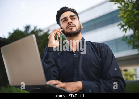 Arabian businessman using laptop computer and talking by phone outside Stock Photo