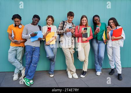 Students isolated in a blue background, using telephones to watch the social media. Stock Photo