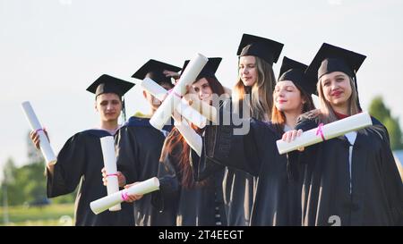 Cheerful graduates waving their diplomas on a sunny day. Stock Photo