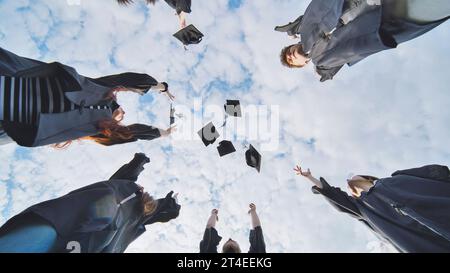 Joyful graduates stand in a circle and toss their caps up. Stock Photo