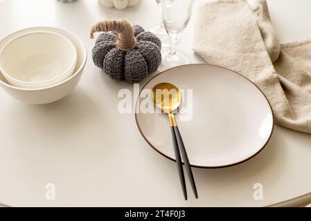 Dinner table setting with white plates and  decorative knite pumpkins on white table top view. Empty modern minimal table setting neutral color Stock Photo