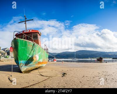 A rusting red, green abd blue fishing boat at low tide on the beach at Barmouth seen on 22 October 2023. Stock Photo