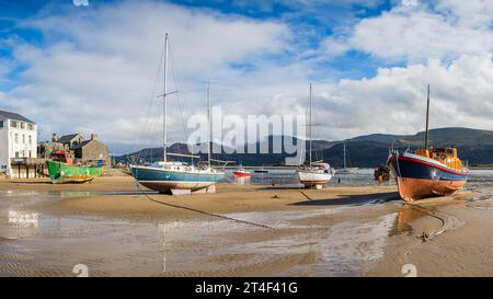 A multi image panorama of various boats beach at Barmouth at low tide backed by the Afon Mawddach estuary and mountains on 22 October 2023. Stock Photo