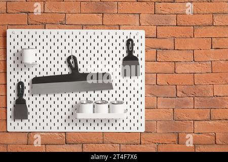 Pegboard with trowels and paint cans on brick wall in workshop Stock Photo
