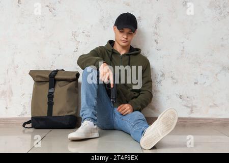 Male student with gun sitting near grunge wall Stock Photo