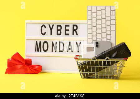 Board with text CYBER MONDAY, gadgets and gift boxes on yellow background Stock Photo