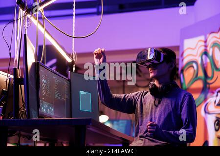 Hacker doing illegal activity in vr headset and exploring metaverse while breaking law. Criminal hacking server in virtual reality simulation while making gestures with hands Stock Photo