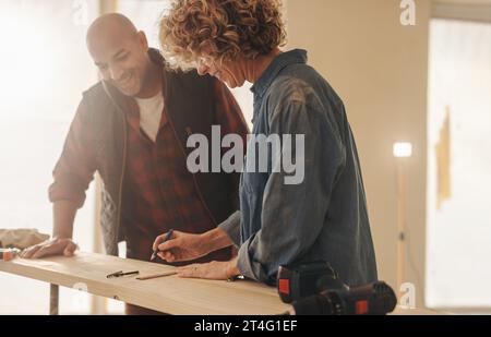 Home owners collaborating on a home renovation project indoors. They discuss and measure a wooden plank, working together in their DIY home improvemen Stock Photo