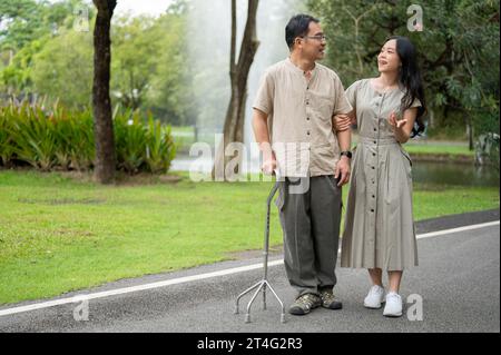 A lovely Asian daughter is enjoying talking with her father while walking in the green park in the morning together. Happy family time concept Stock Photo
