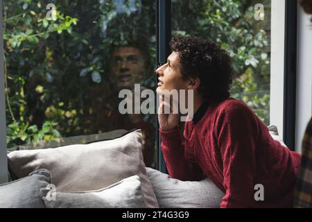 Happy biracial man with curly hair looking through window at home Stock Photo