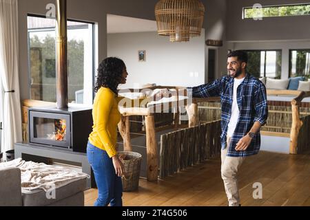 Happy biracial couple dancing and smiling in living room at home Stock Photo