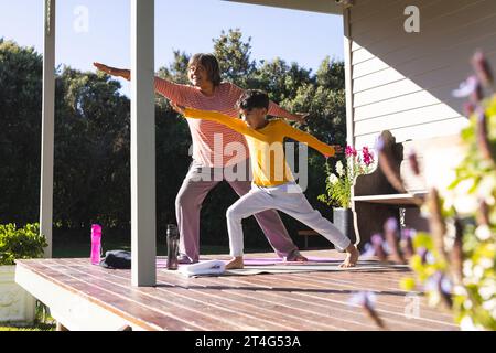 Happy biracial grandmother and grandson doing yoga and stretching in garden Stock Photo