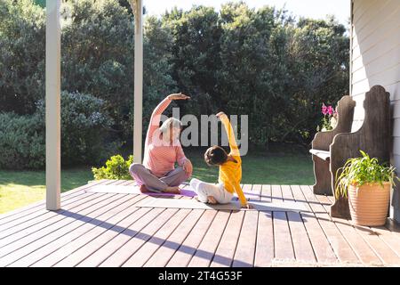 Happy biracial grandmother and grandson doing yoga and stretching in garden Stock Photo