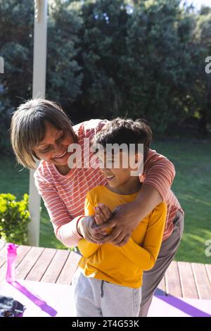 Happy biracial grandmother and grandson doing yoga and meditating in garden Stock Photo