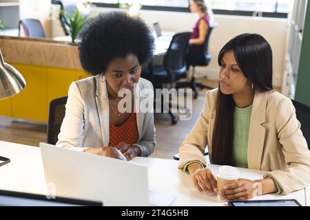 Busy diverse female colleagues discussing work with laptop in office Stock Photo