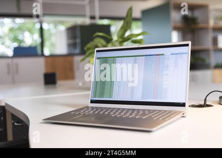 Empty creative office with wooden furniture, plants and laptop with data on table Stock Photo