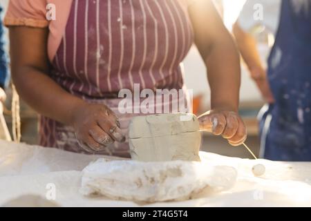 Mid section of african american female potter cutting clay with wire in pottery studio Stock Photo