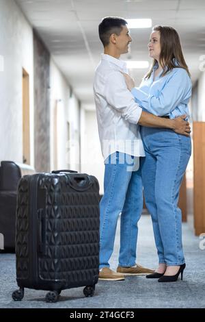 Young couple stands hugging in illuminated hotel hallway Stock Photo
