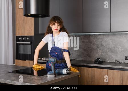 Pleased woman in overalls has finished assembling kitchen furniture Stock Photo