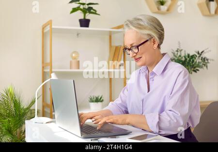 Middle aged business woman sitting at desk in her office and typing on laptop computer Stock Photo
