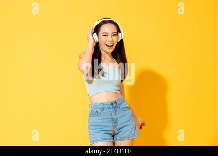 Young pretty Asian woman wearing headphones listening to music and dancing in the studio yellow color background Stock Photo