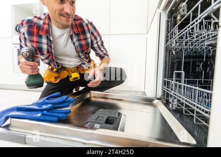Worker using screwdriver to repair dishwasher at home stock photo Stock Photo