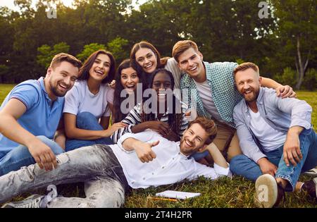 Portrait of cheerful students posing while sitting in park on grass in summer. Stock Photo