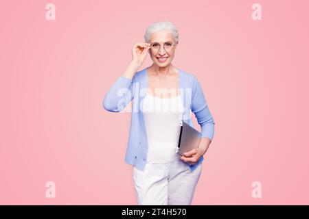 Grey haired old smiling business woman wearing glasses, holding tablet. Isolated over violet purple background Stock Photo