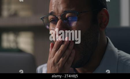 Tired exhausted bored adult Indian man American manager yawn need sleep lack energy insomnia sleeping disorder overtime computer work in office Stock Photo