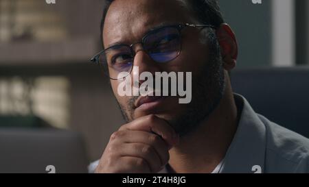 Close up Indian man in glasses Arabian businessman with laptop thinking holding chin pensive thoughtful employer think pondering idea solving problem Stock Photo