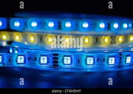 Bobbin with roll of glowing LED strip lighting placed on table, blue and warm white color in dark room Stock Photo
