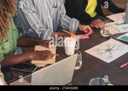 A group of professionals gather around a table, engaging in a brainstorming session. Hands gesture towards charts, post-its, and a mind map, highlight Stock Photo