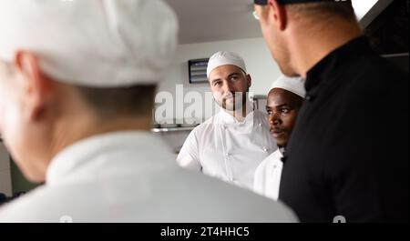 Diverse male students looking and listening to chef teacher in commercial kitchen at cooking school Stock Photo
