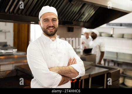 Portrait of smiling caucasian male chef in white uniform standing in kitchen at cooking school Stock Photo
