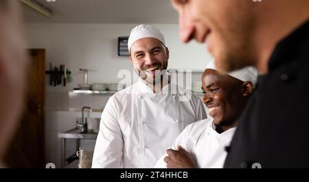 Diverse male students laughing and learning cooking from chef teacher in commercial kitchen Stock Photo