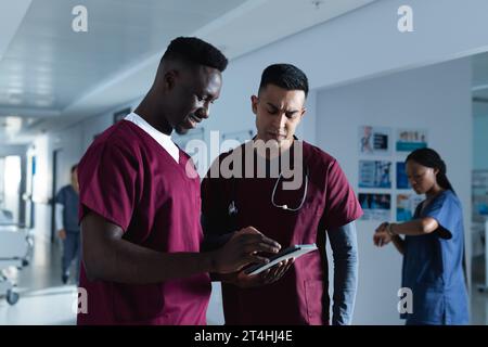 Diverse male doctors discussing work, using tablet in corridor at hospital Stock Photo